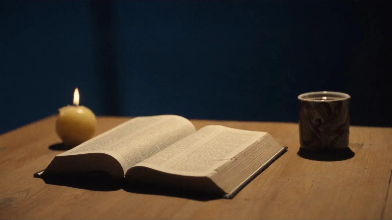 An open Bible beside a lit candle on a wooden table