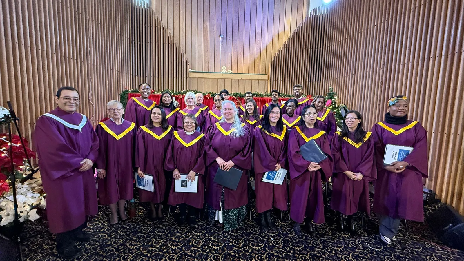 Edmonton Central choir members in maroon and gold robes in the sanctuary with Christmas poinsettias and garland