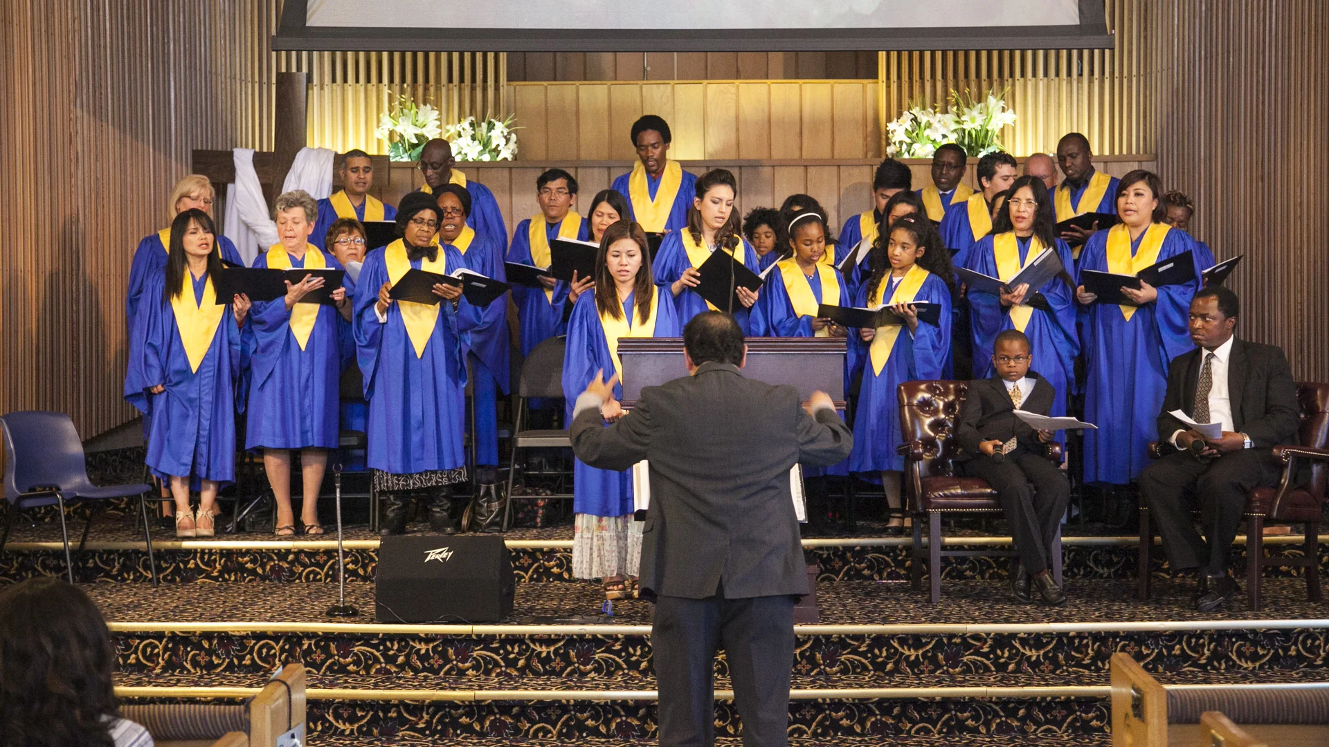 The Edmonton Central choir in blue and gold robes singing in the sanctuary while the director conducts