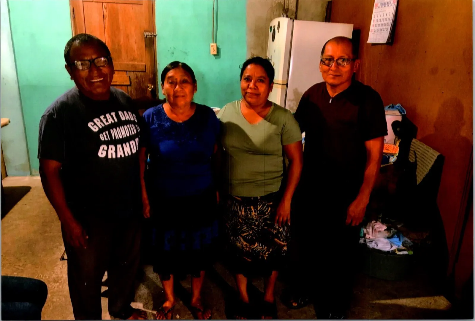Four adults standing together and smiling inside a home with turquoise walls
