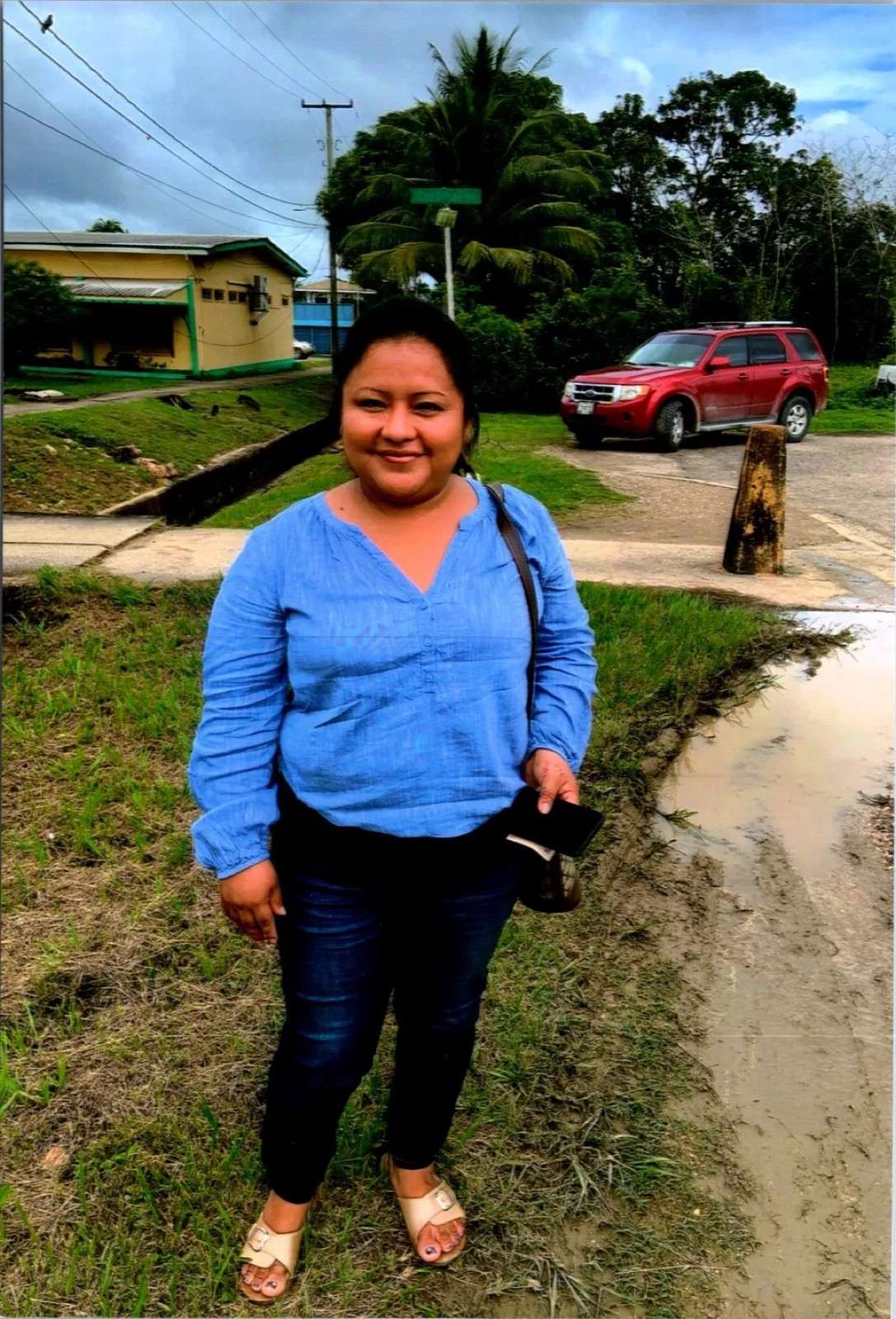 A woman in a blue blouse standing beside a road in Belize after rain